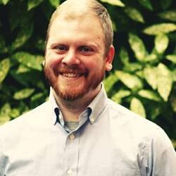 David LeGault is wearing a button-up shirt and smiles with teeth.